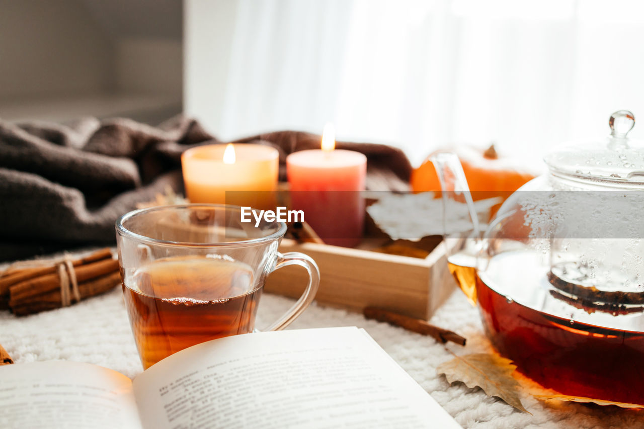 Autumn mood, a burning candle, a book and a kettle of hot tea on a cozy plaid. atmospheric