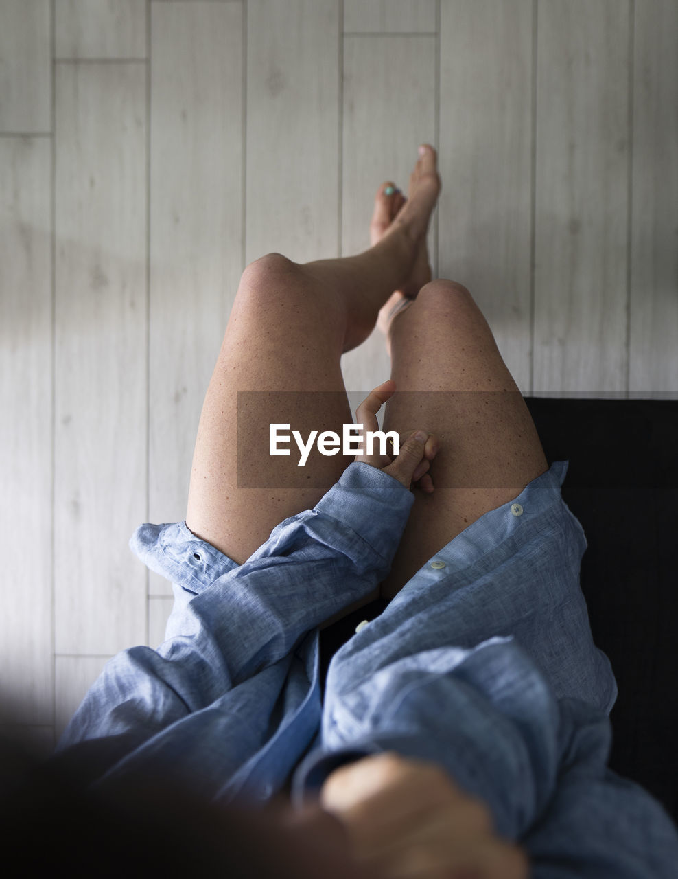 LOW SECTION OF MAN SITTING ON SOFA AT HOME