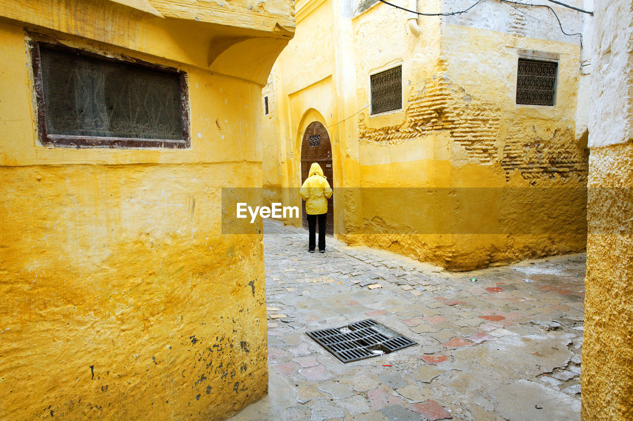 Rear view of man walking at alley amidst houses