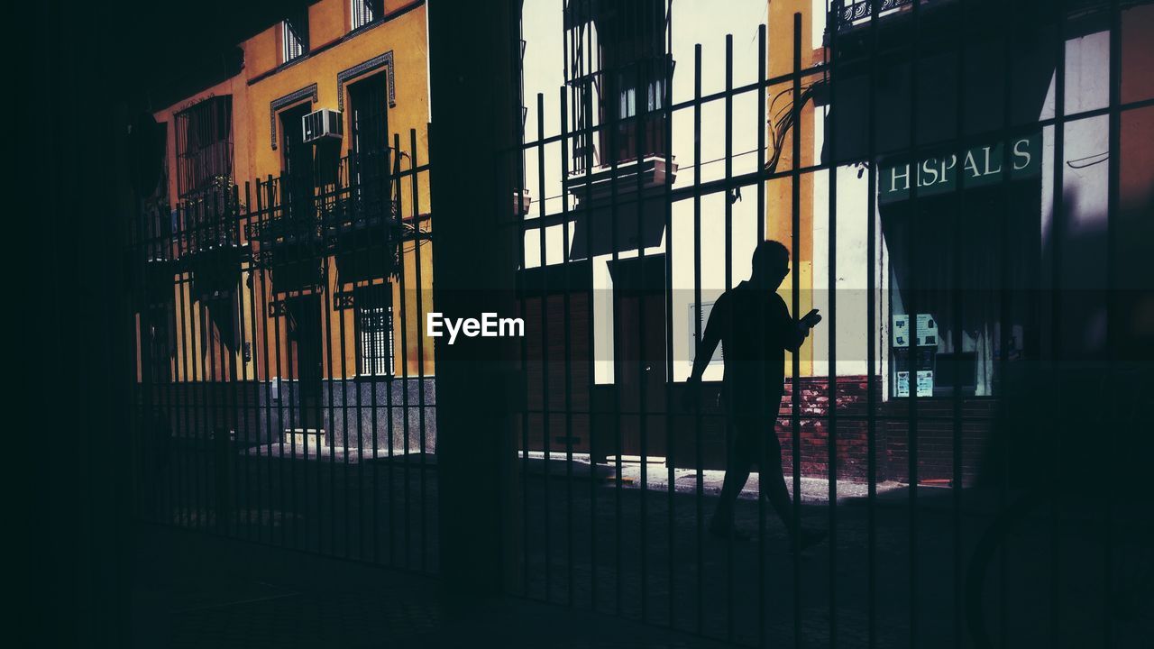 Silhouette man walking on sidewalk by buildings