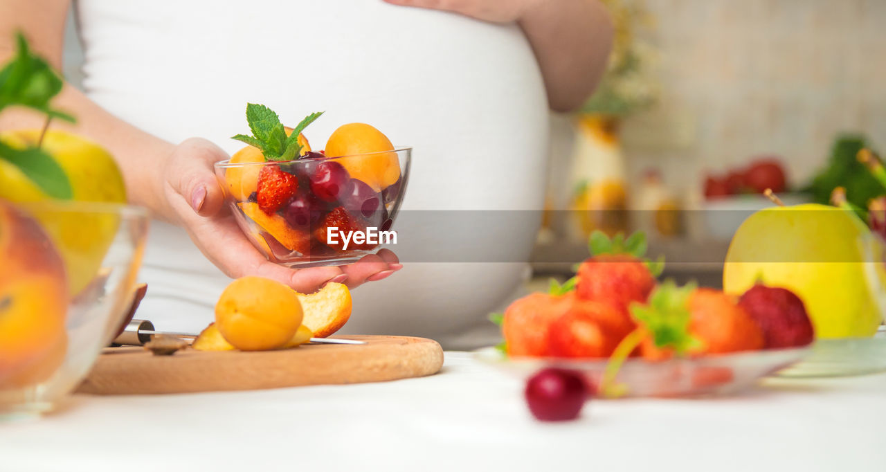 Midsection of pregnant woman with bowl of fruits