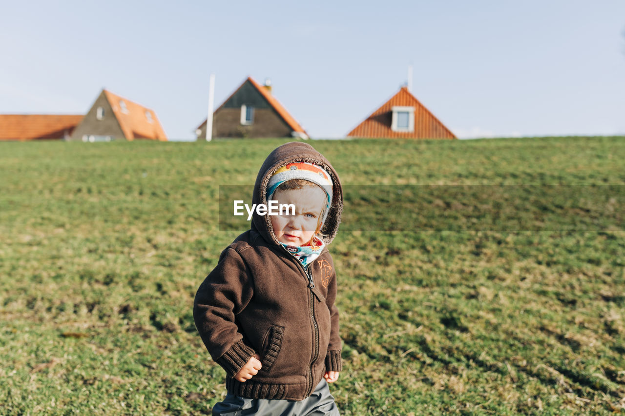 Cute girl wearing warm clothing standing on field during sunny day