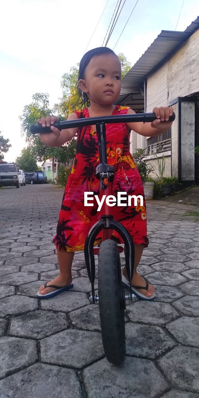 PORTRAIT OF A GIRL RIDING BICYCLE ON FOOTPATH