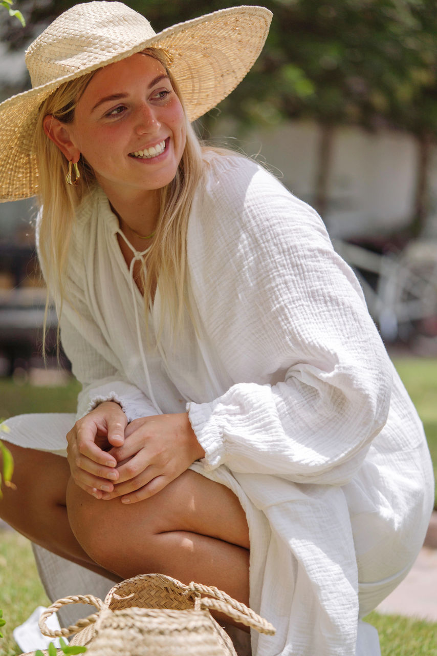 Woman wearing straw hat and a white dress picking red chilies in the garden