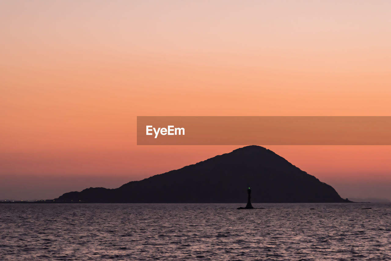 Silhouette island by sea against orange sky