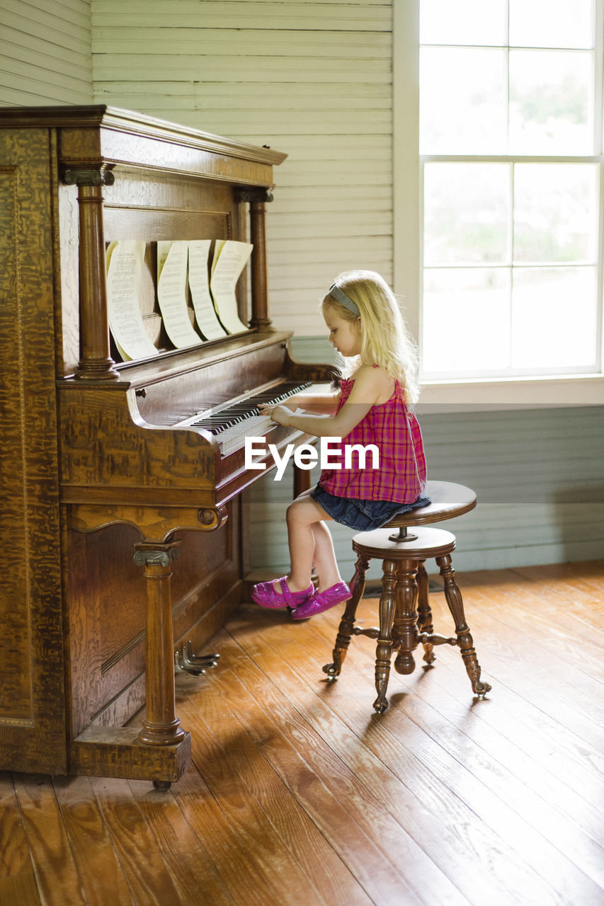 Side view of girl playing piano while sitting on stool at home