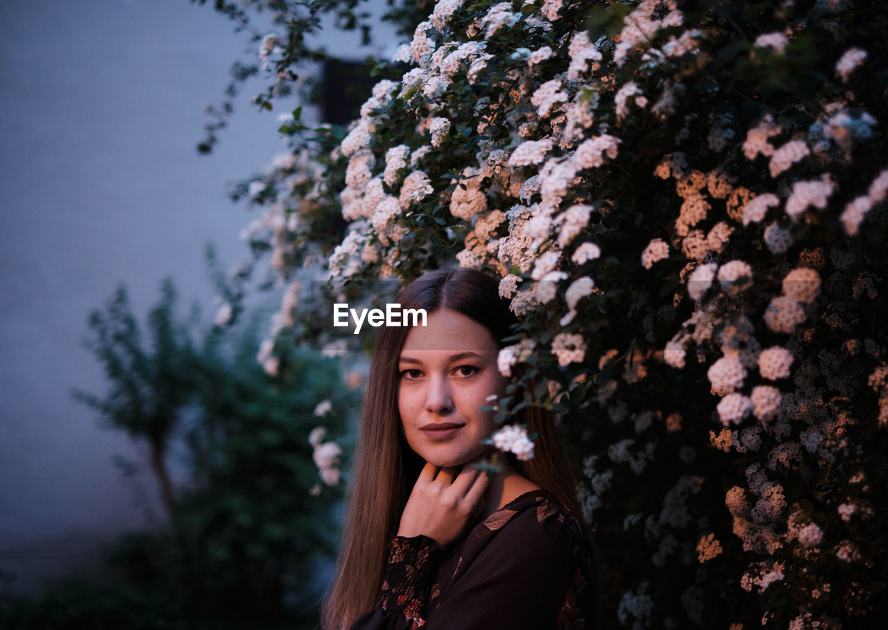 Portrait of young woman standing by plants in park at night