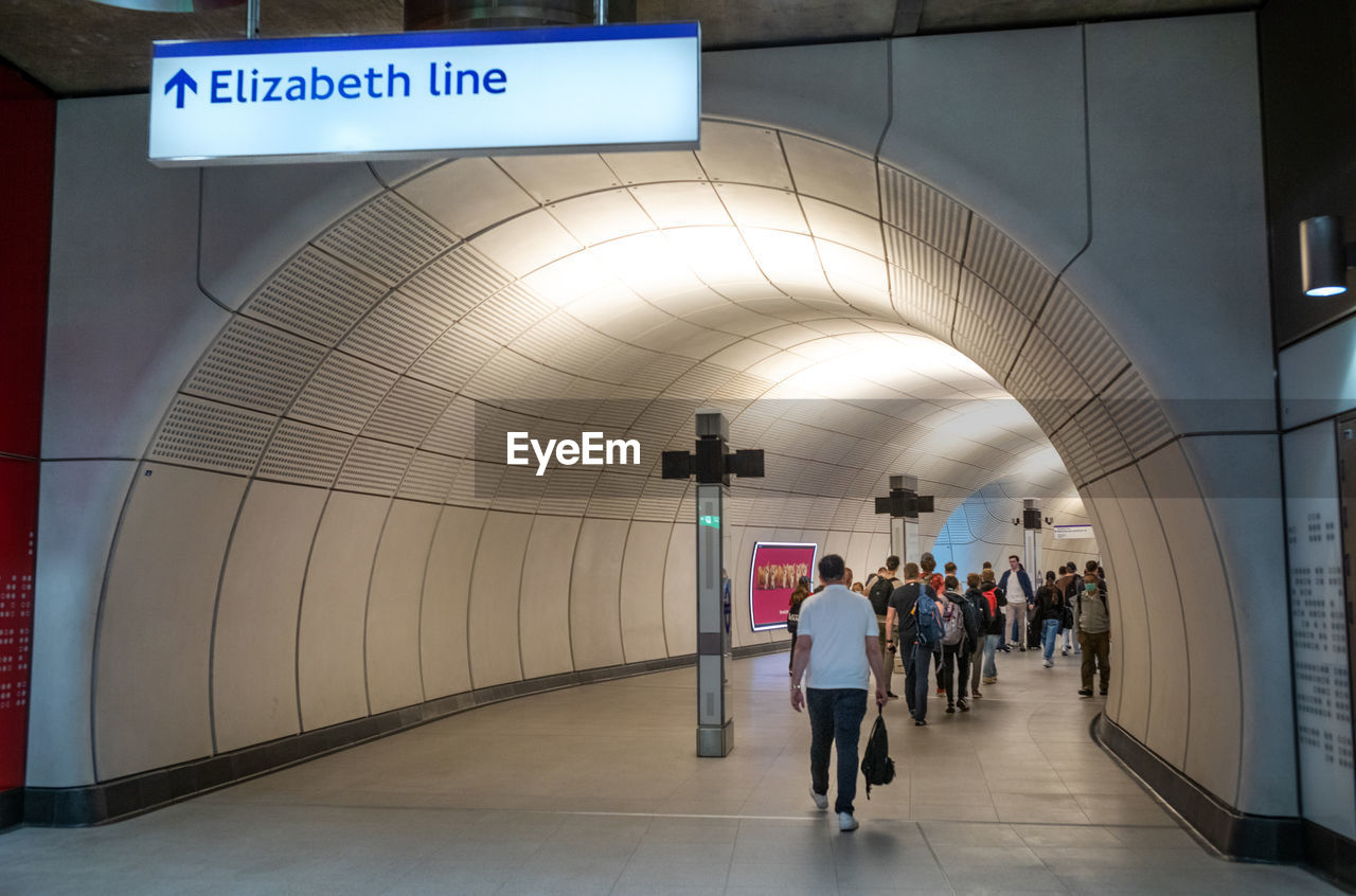 architecture, metro station, group of people, travel, transportation, public transport, subway station, sign, indoors, communication, transport, subway, walking, adult, text, public transportation, mode of transportation, men, infrastructure, full length, tunnel, arch, built structure, city, information sign, journey, tourism, women, travel destinations, crowd, tourist, passenger, city life, rail transportation, airport, illuminated