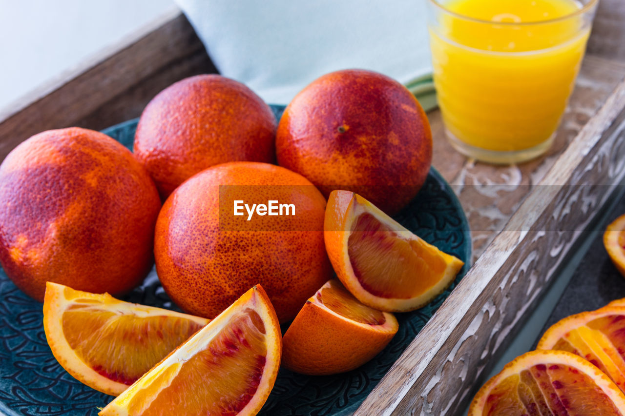 Blood oranges whole and sliced on plate and tray with glass of orange juice in background