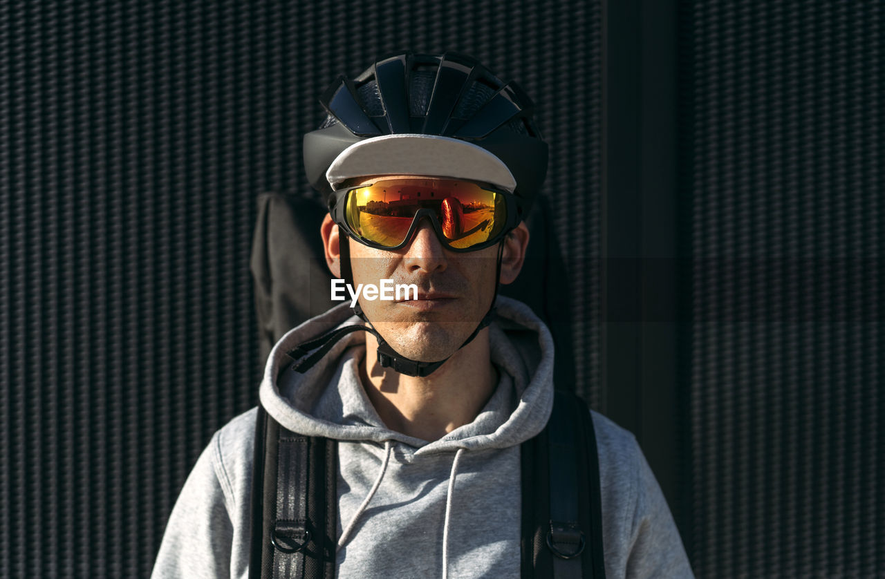 Delivery man with backpack standing in front of black wall