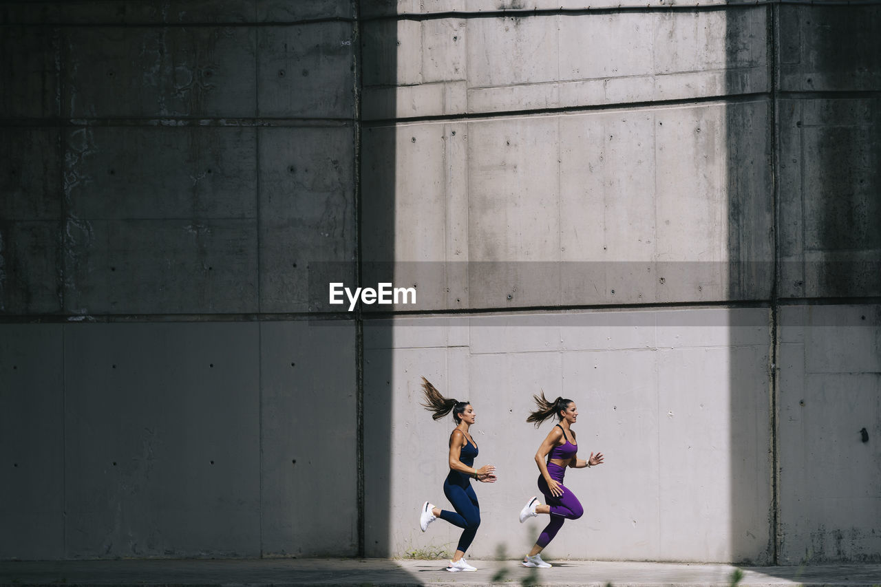 Twin sisters running on footpath by wall