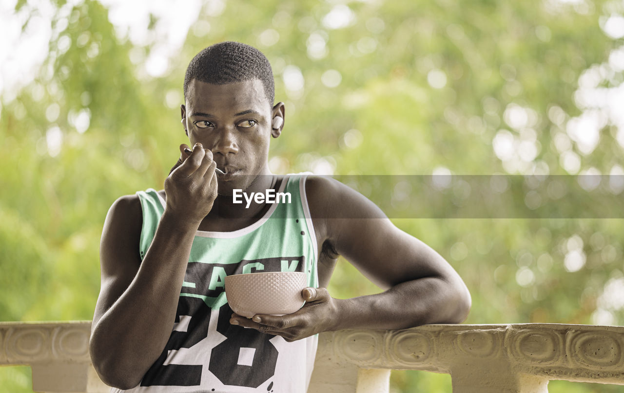 African american male with bowl of fruits listening to music and looking away while having breakfast