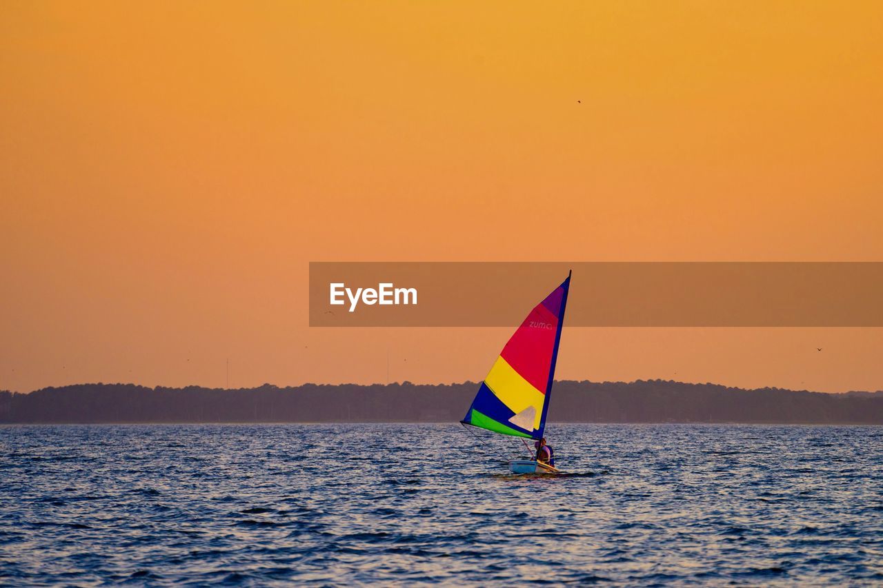 SAILBOAT ON SEA AGAINST ORANGE SKY