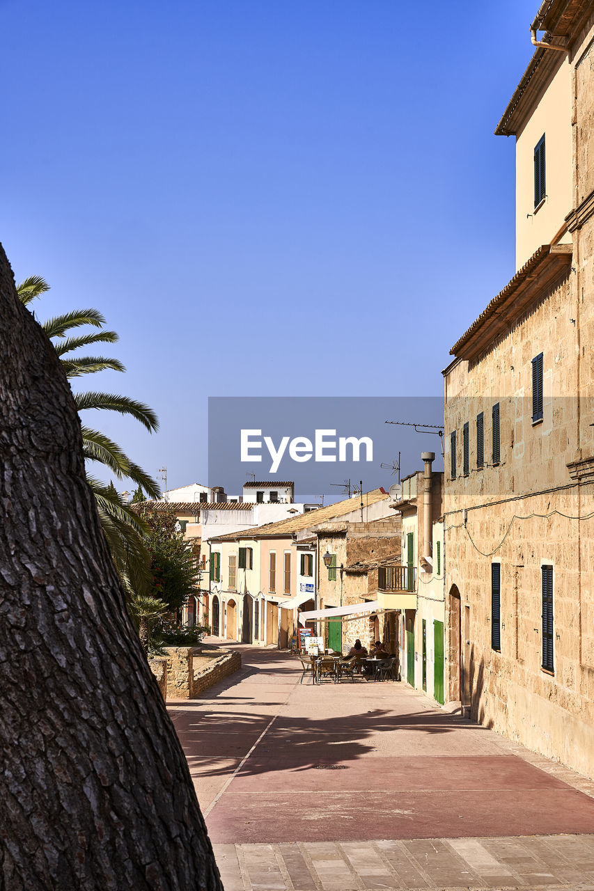 Street amidst buildings against clear blue sky