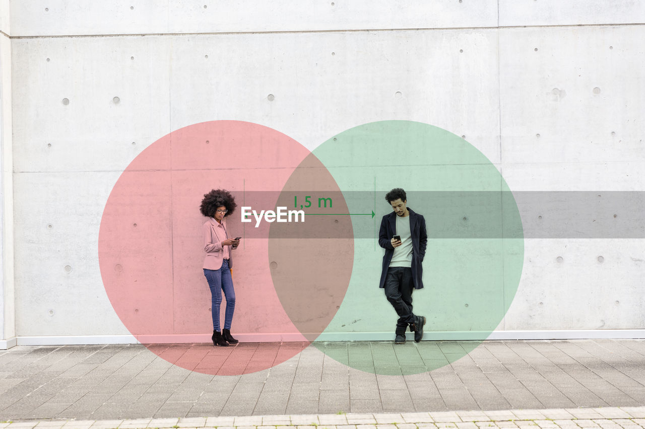 Two overlapping circles visualizing social distancing covering man and woman standing outdoors with smart phones in hands