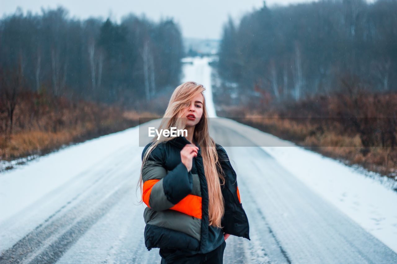 Portrait of young woman standing on snow covered road