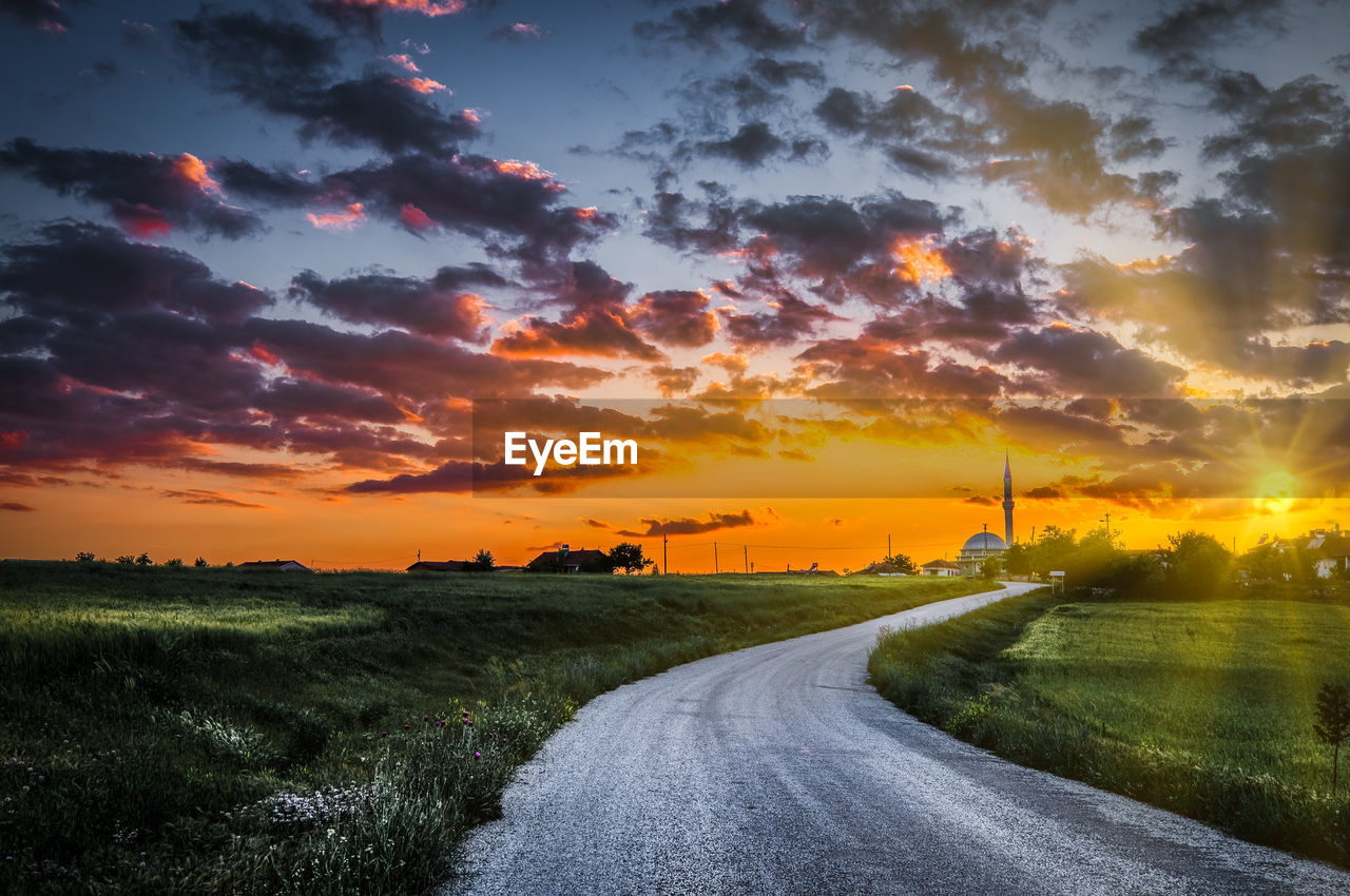 Road amidst field against sky during sunset