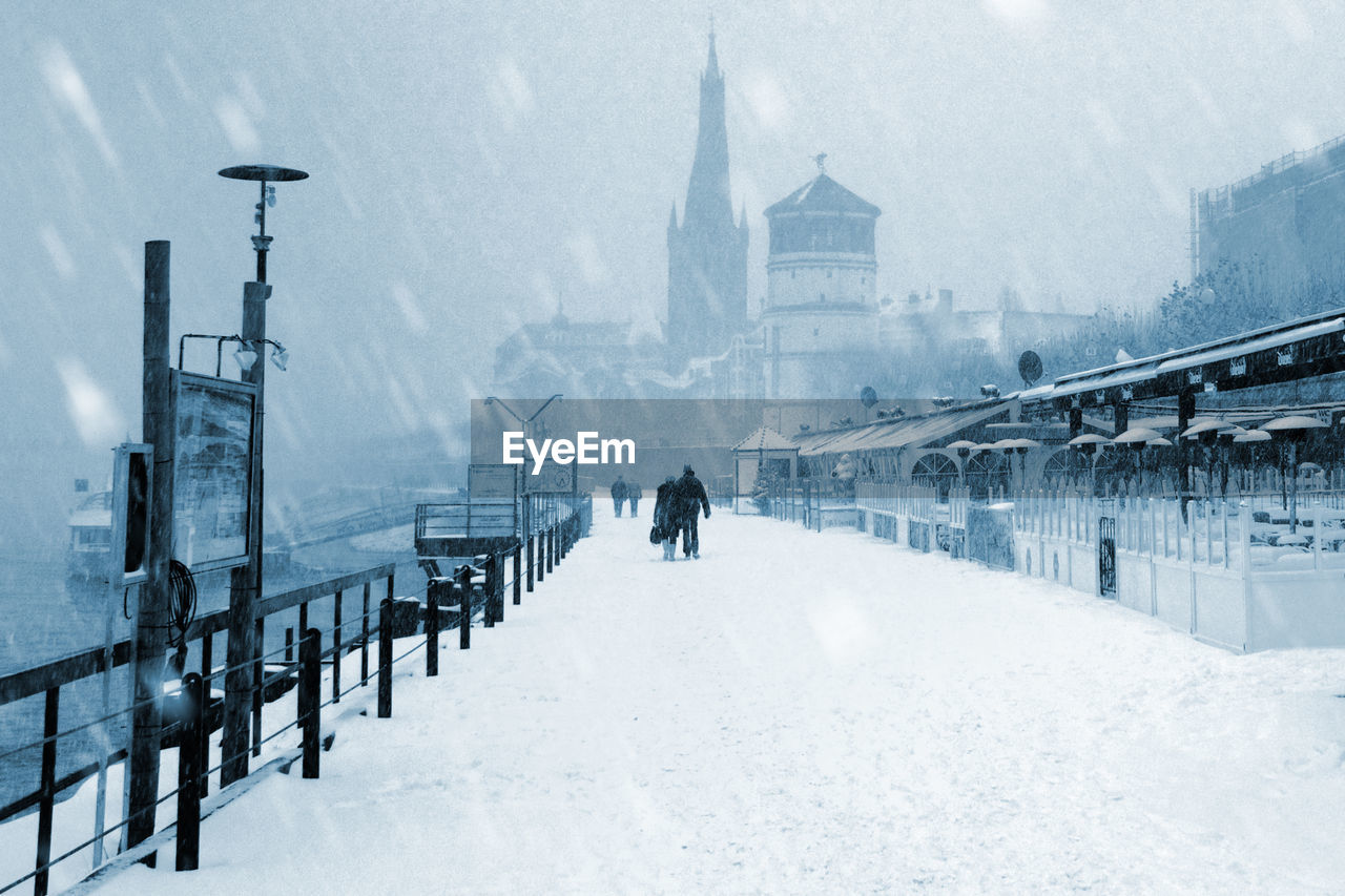 Rear view of people walking on snow covered street in city during winter