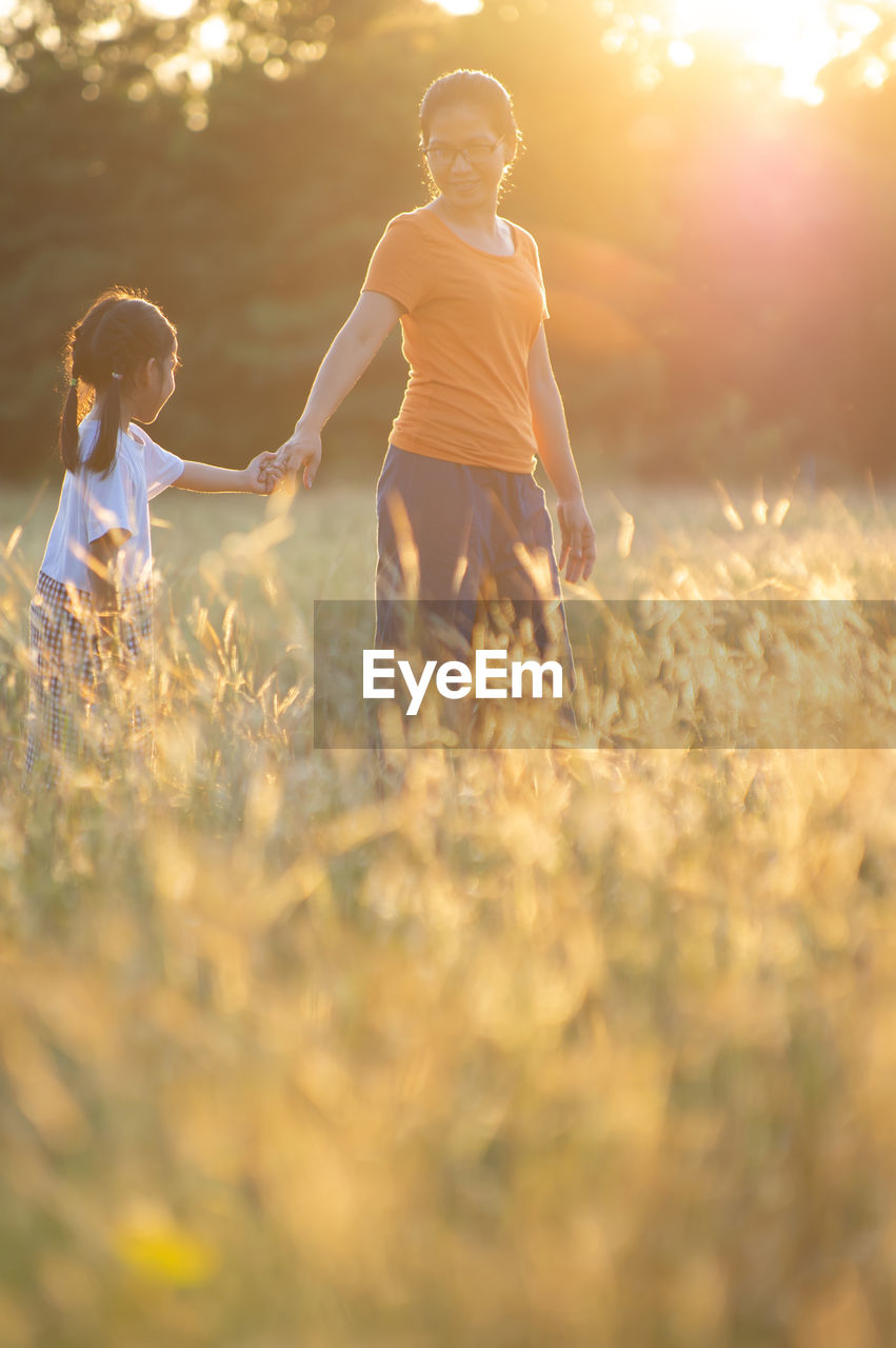 Mother with daughter standing amidst plants on field during sunset