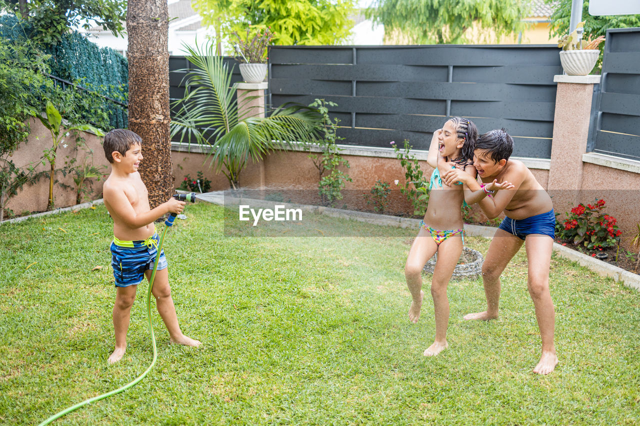 Three funny kids playing with a hose in the garden