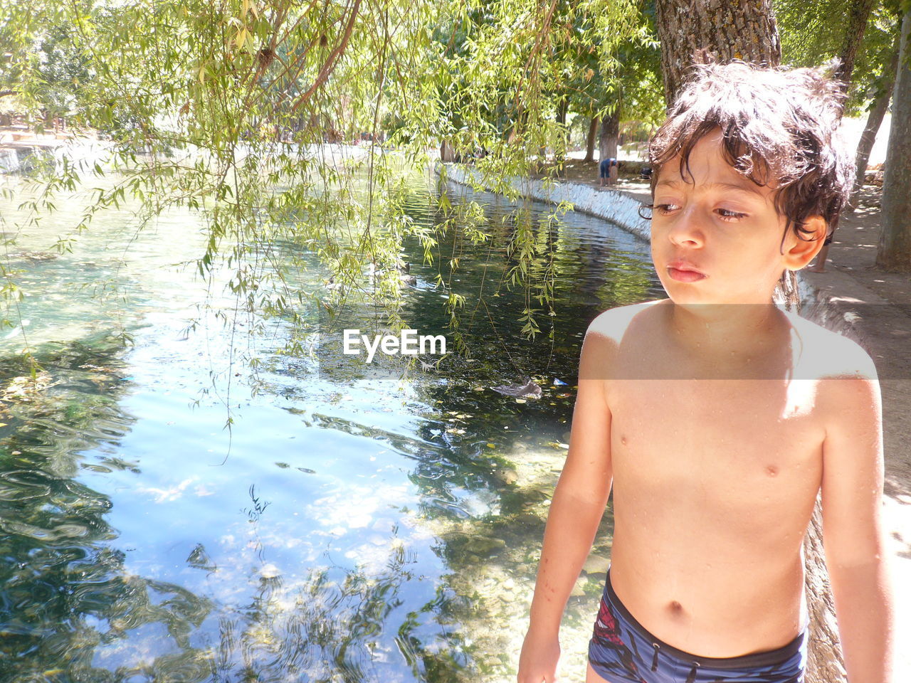 Cute shirtless boy standing against pond