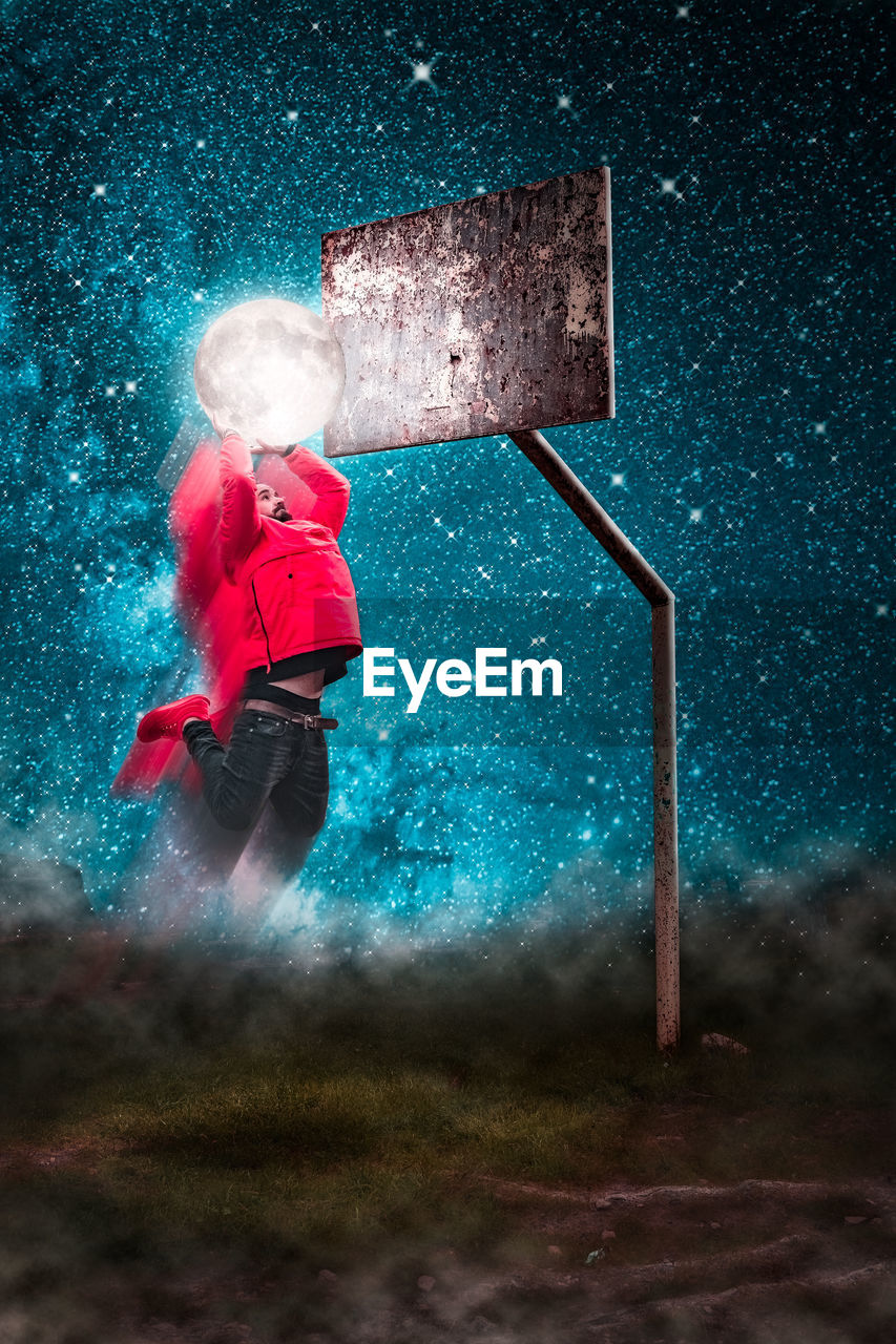 Optical illusion of man dunking moon in basketball hoop against sky