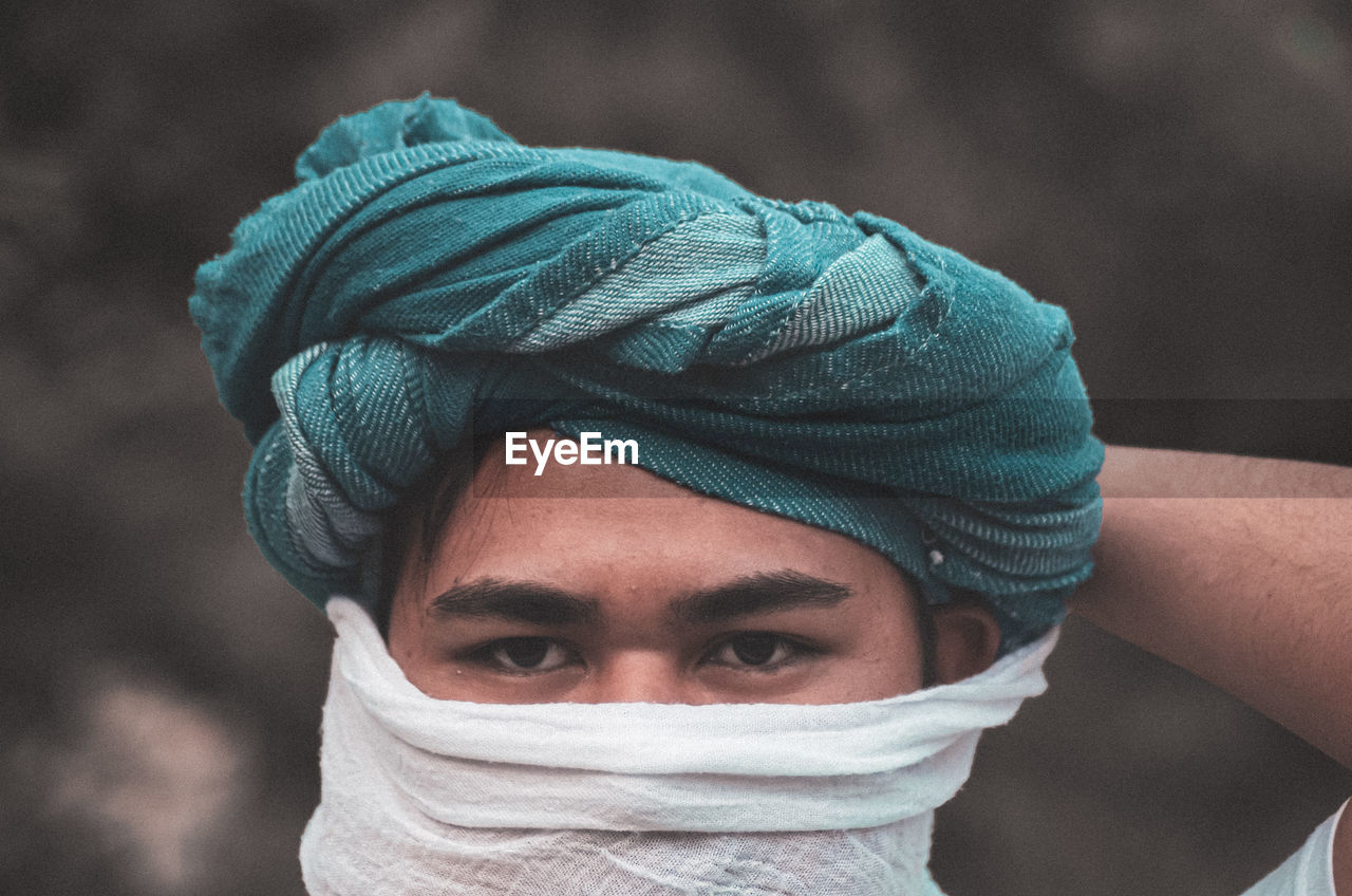 Close-up portrait of man covering face with scarf while wearing turban
