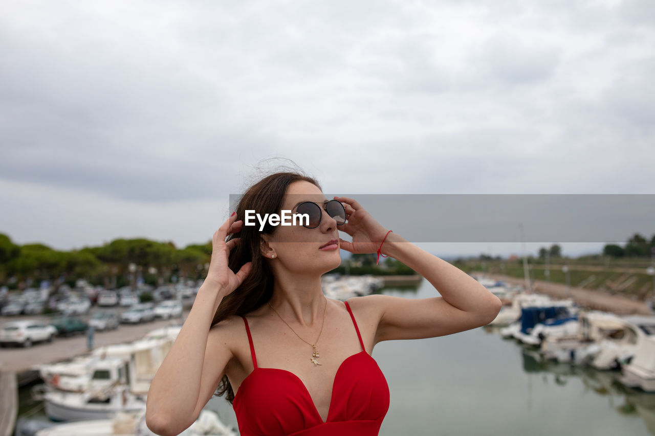 Woman wearing sunglasses while standing against boats moored at harbor