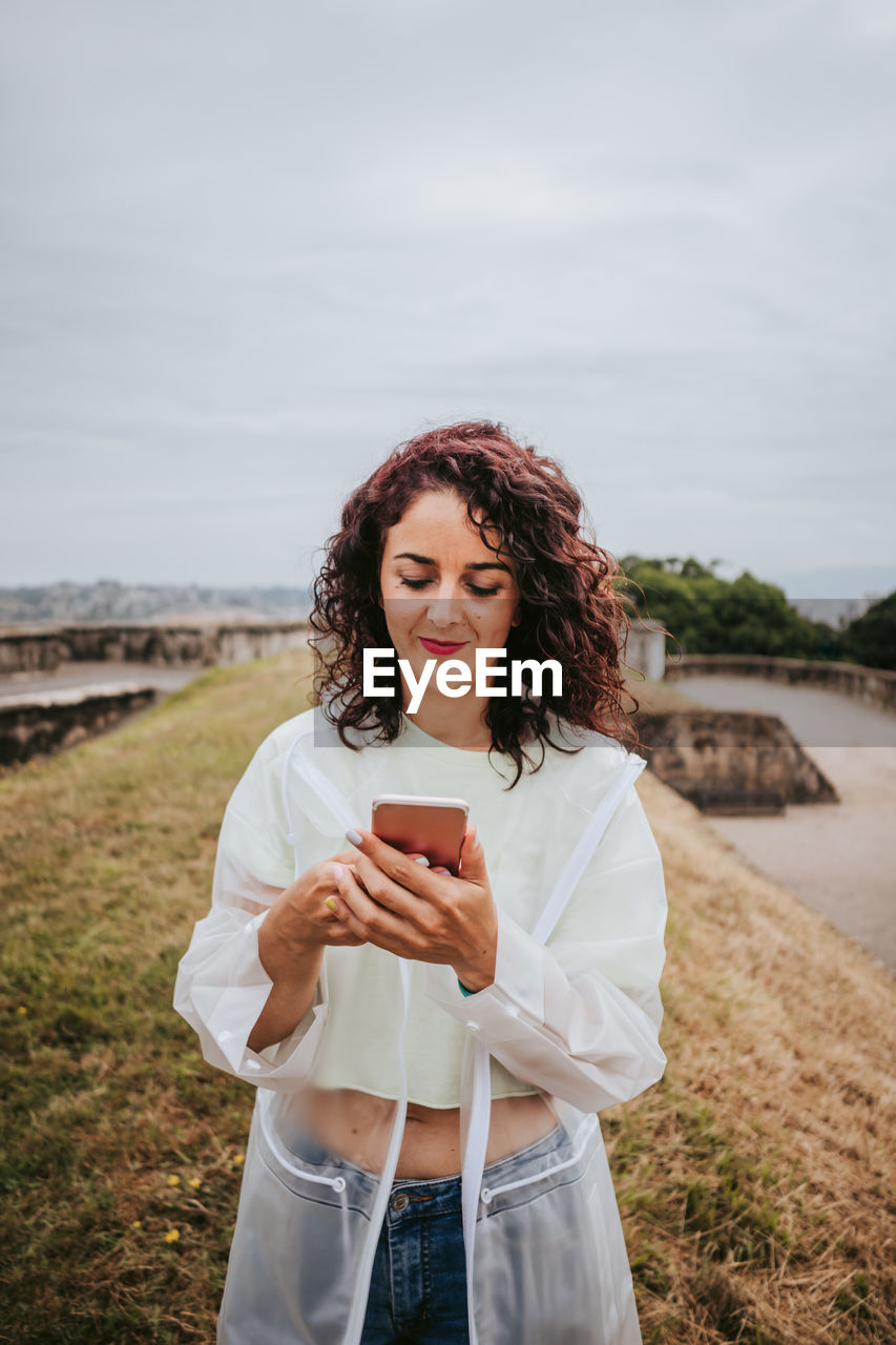 Full length of young woman using mobile phone against sky