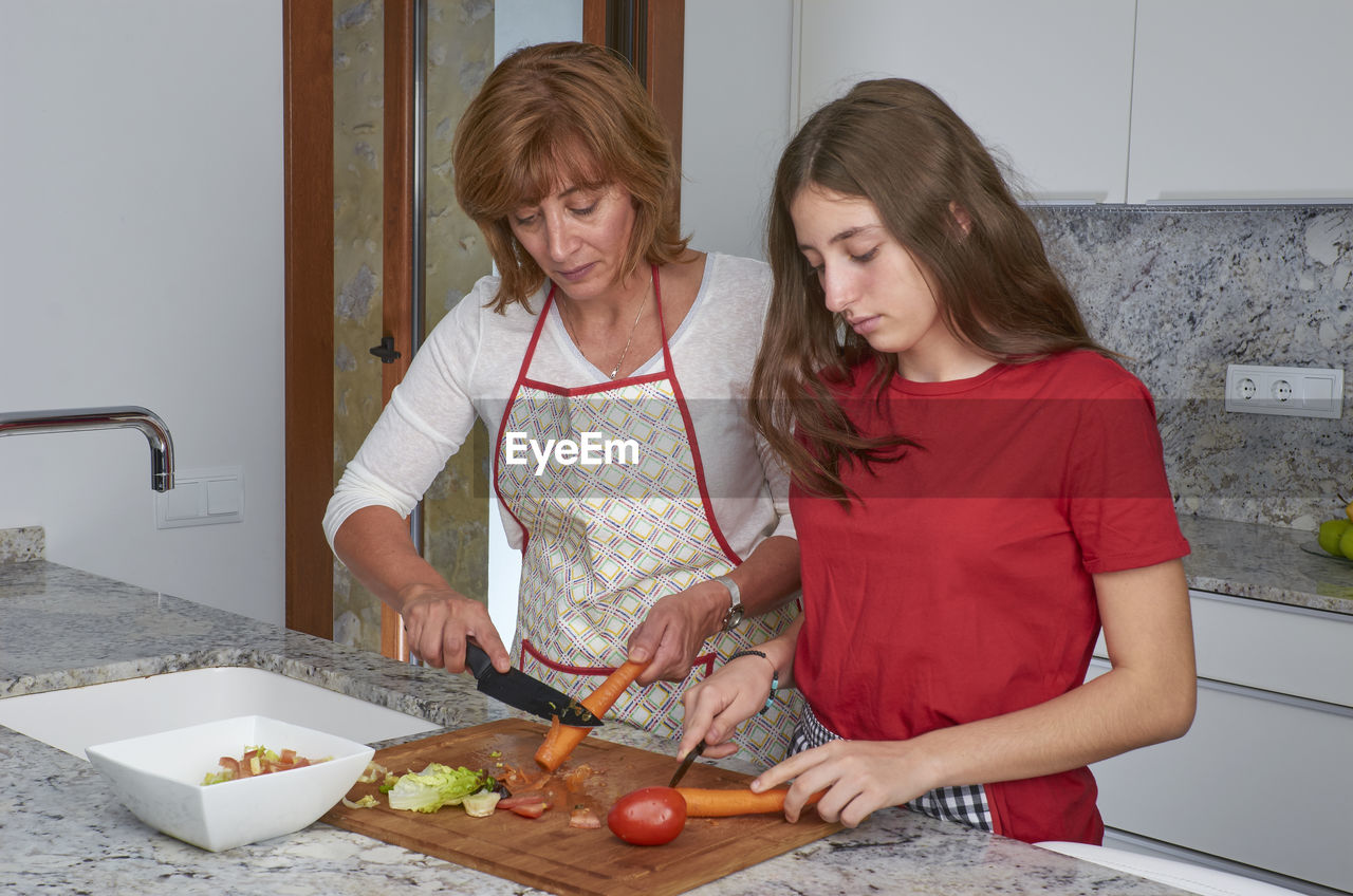 Mother and daughter preparing salad in kitchen at home