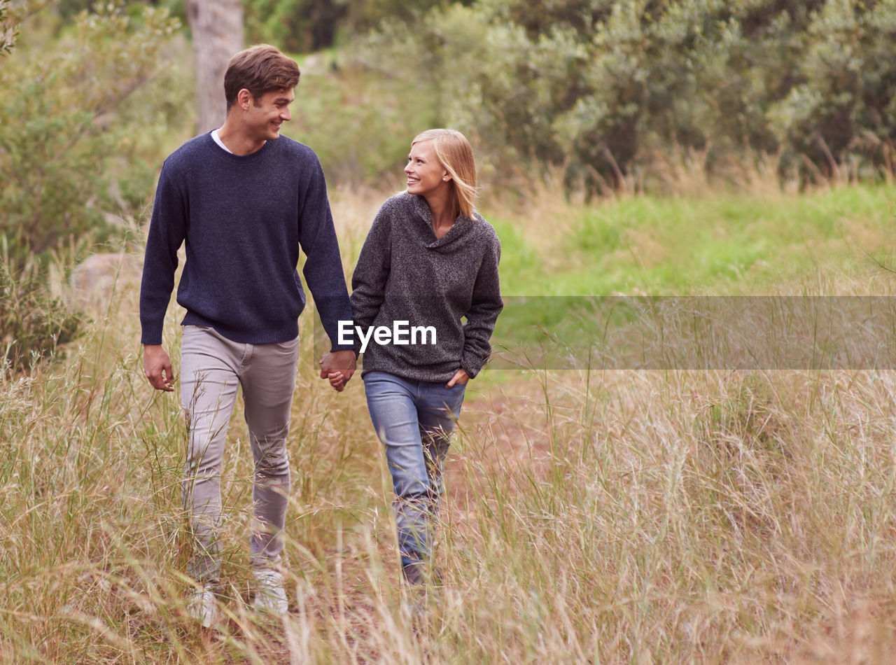 two people, togetherness, adult, men, plant, grass, women, casual clothing, emotion, positive emotion, walking, nature, love, bonding, land, lifestyles, leisure activity, field, happiness, landscape, holding hands, female, day, young adult, full length, rural scene, smiling, outdoors, person, rear view, friendship, meadow, prairie, clothing, carefree, mature adult, non-urban scene, romance, tree, jeans, three quarter length, enjoyment