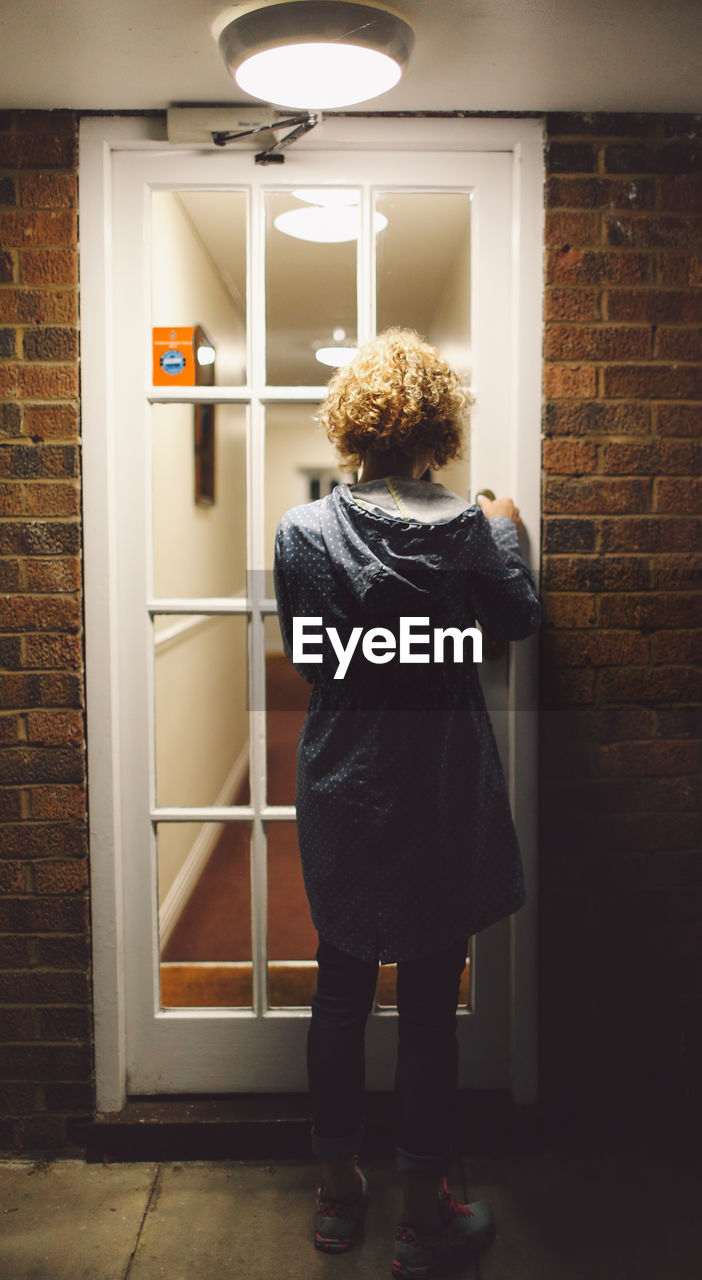 Full length rear view of woman standing by illuminated door