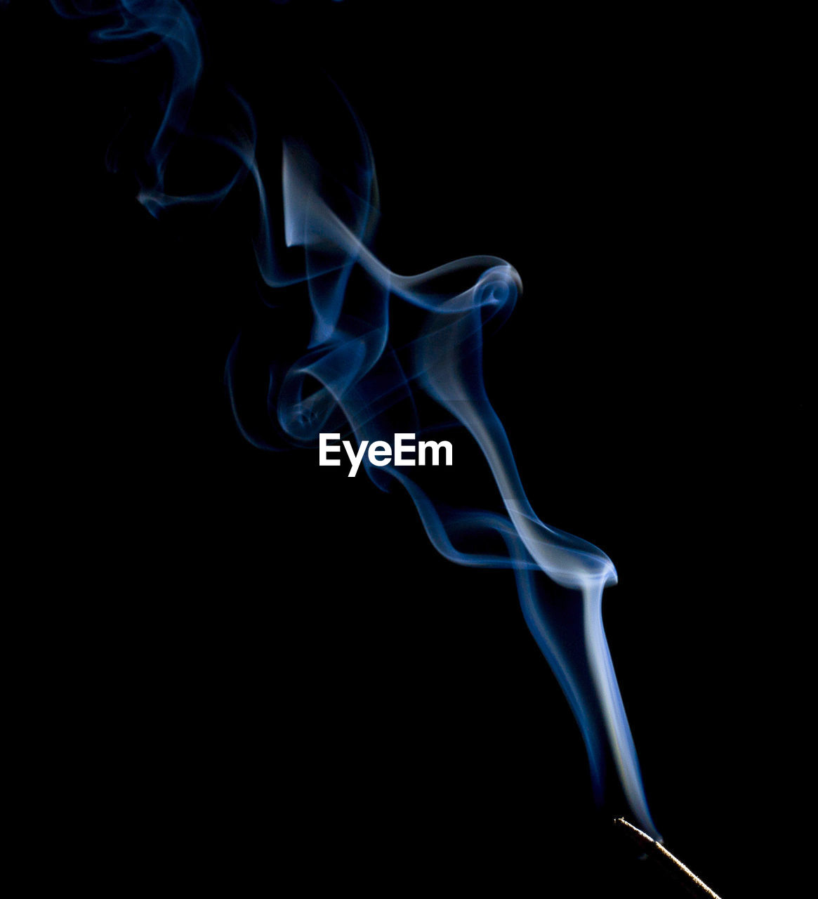 Incense stick emitting smoke against black background