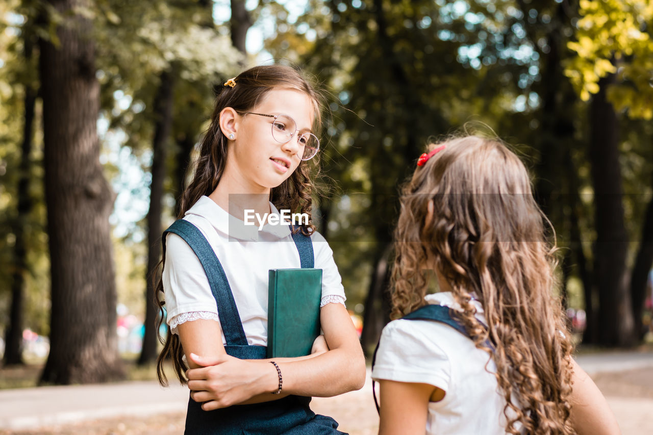 Two female students in school uniforms are talking in the park on a warm day