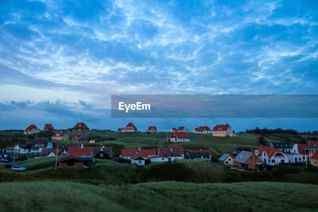 Houses on field by town against sky