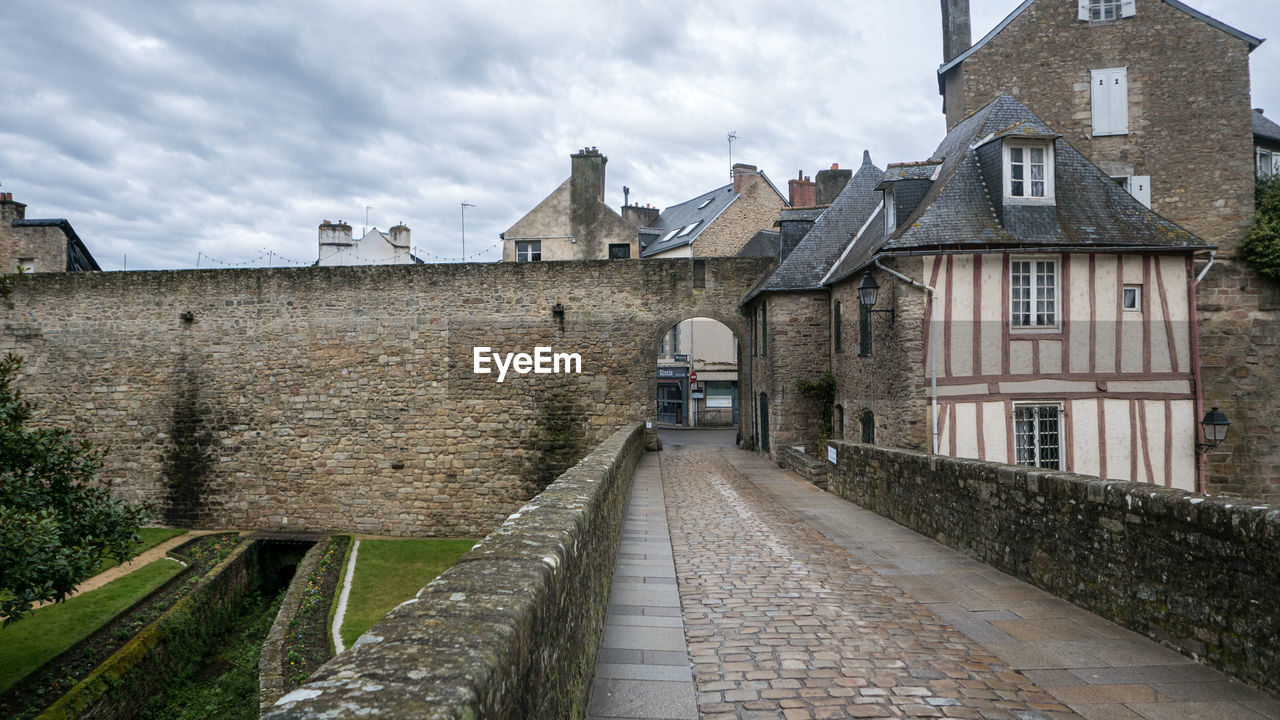 FOOTPATH AMIDST OLD BUILDINGS AGAINST SKY