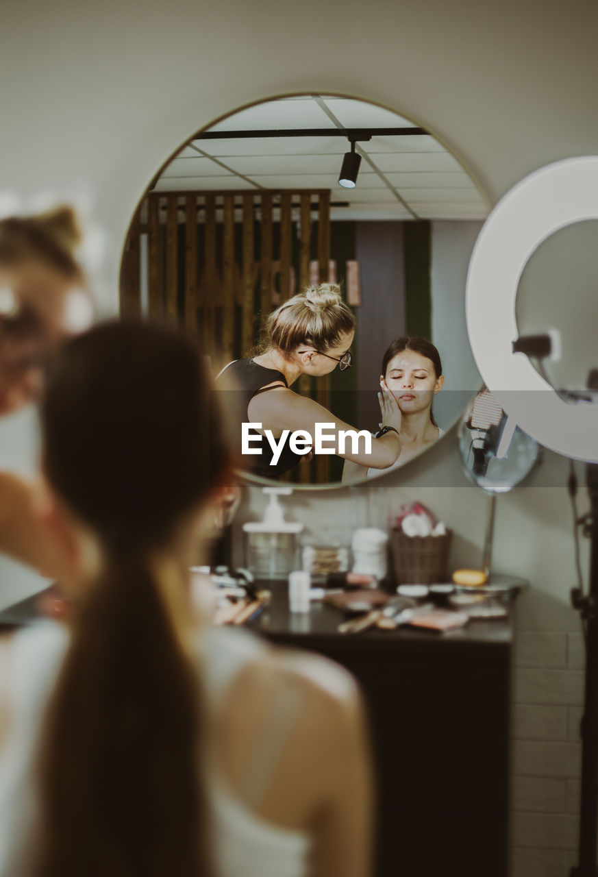 A young makeup artist applies protective cream to a girl s face.