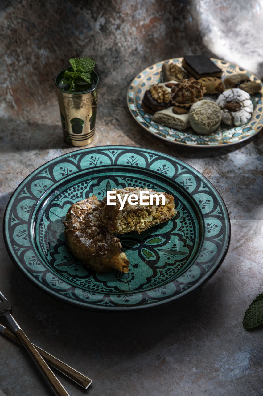 From above of baklava and biscuits with moroccan peppermint tea near knife and fork placed on table decorated with mint leaves