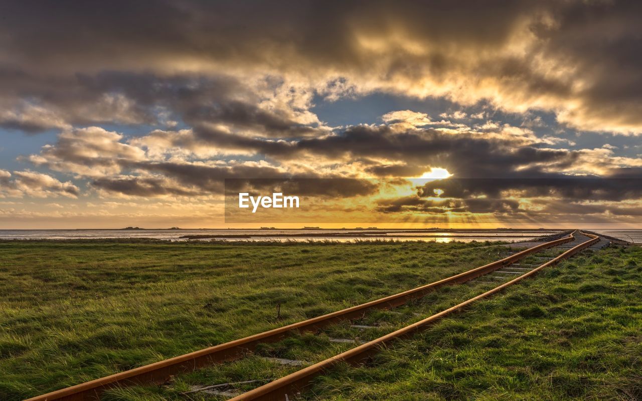 Railroad tracks on field against cloudy sky during sunset