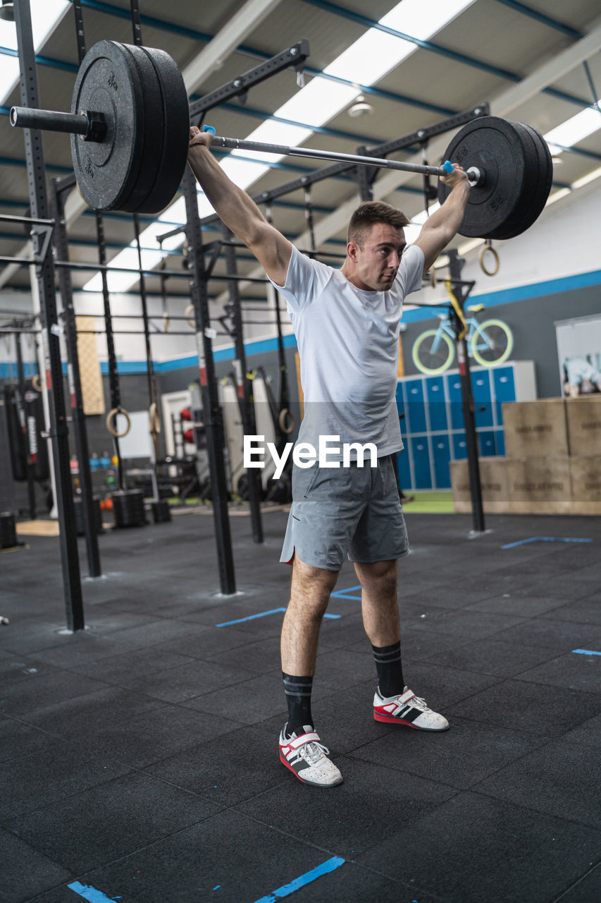 Confident sportsman holding barbell with weights in gym