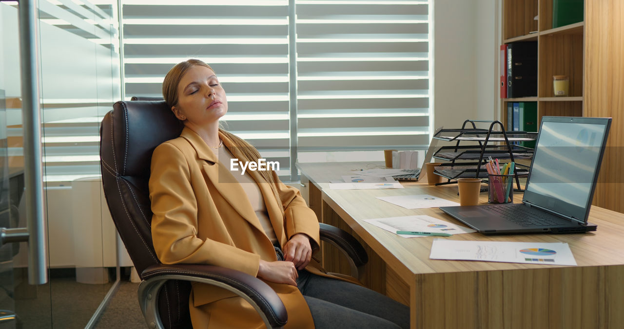 Tired business woman lying on chair and closing her eyes after hard working day. 