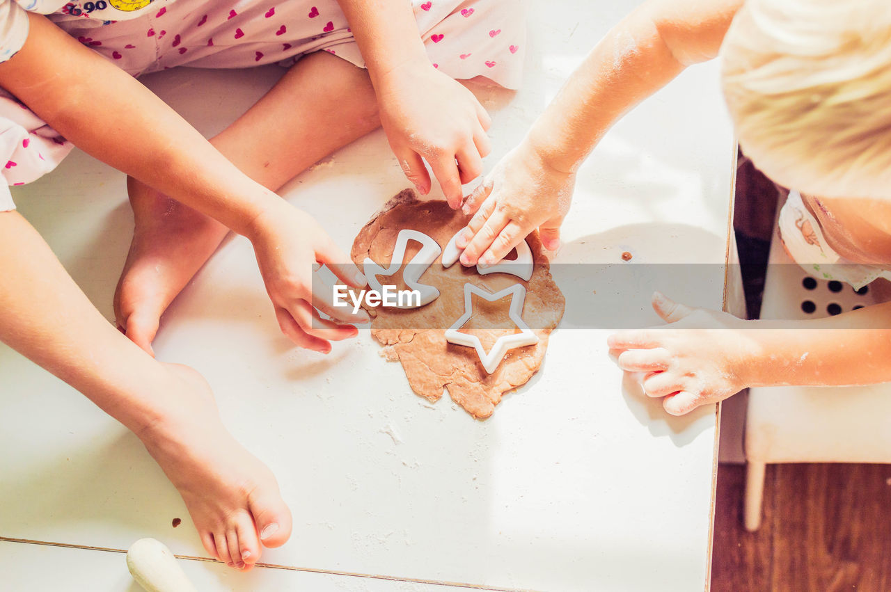 High angle view of siblings cutting pastry with cutter on table