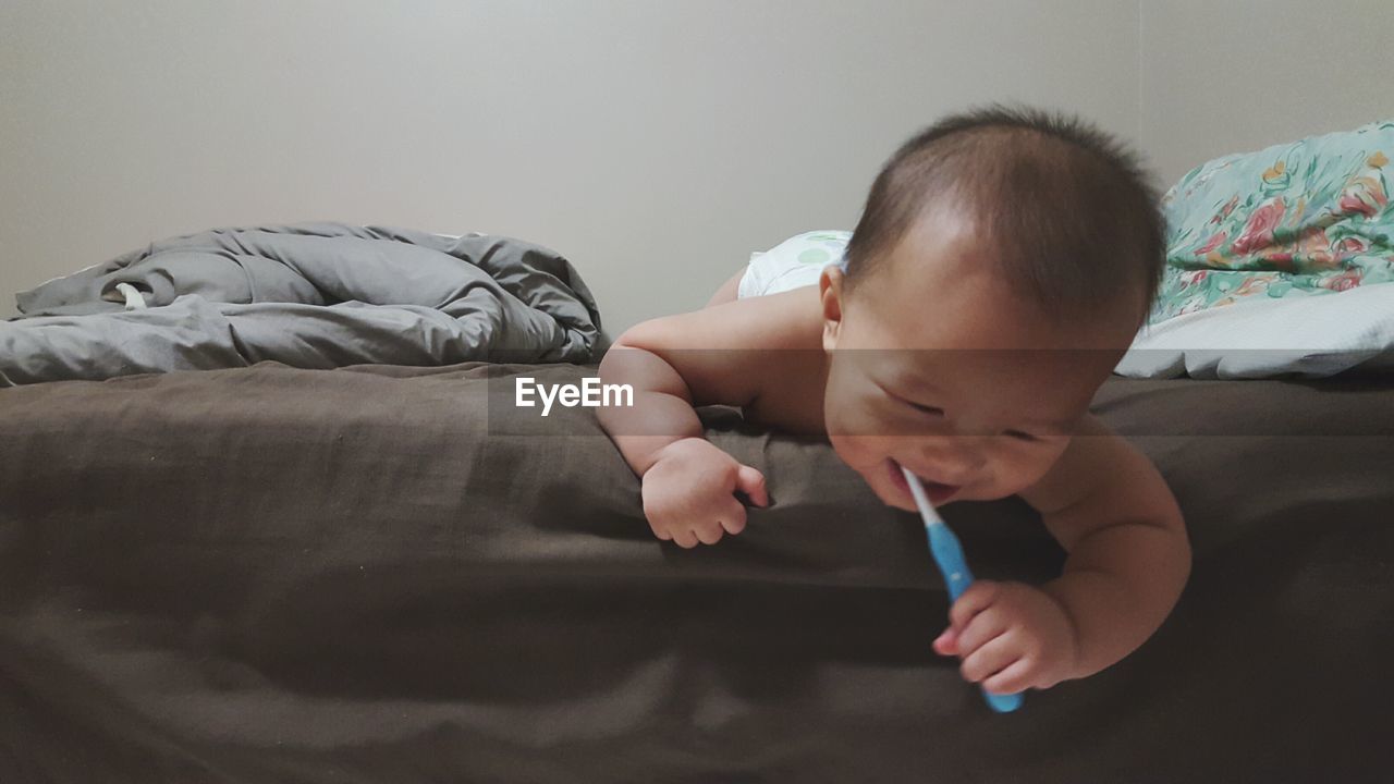 Cute baby boy with toothbrush lying on bed at home