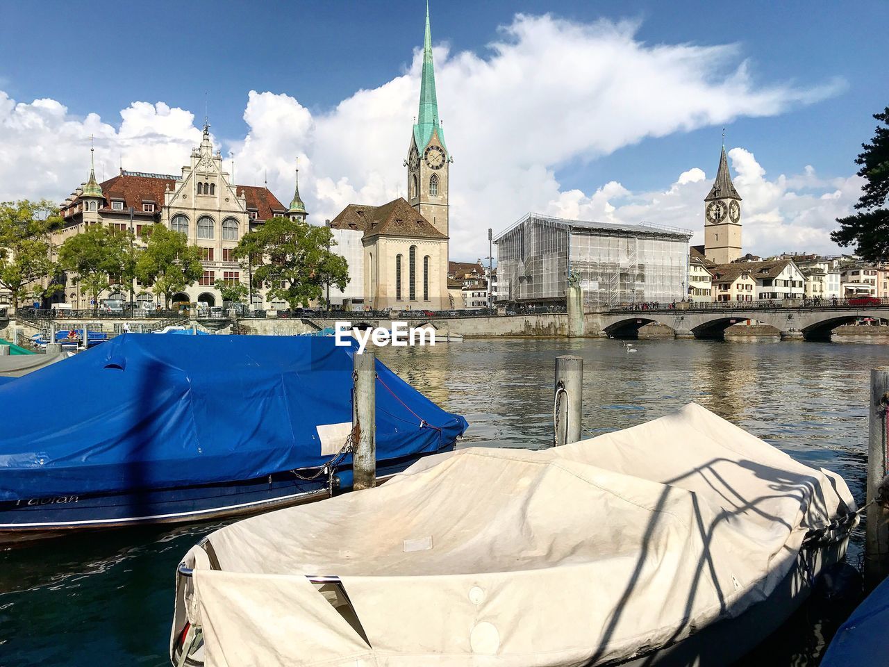 Covered boats moored on river in city against sky