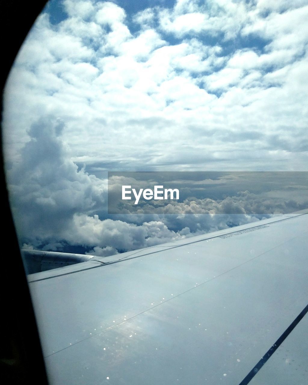 AERIAL VIEW OF AIRPLANE WING OVER CLOUDS SEEN FROM WINDOW