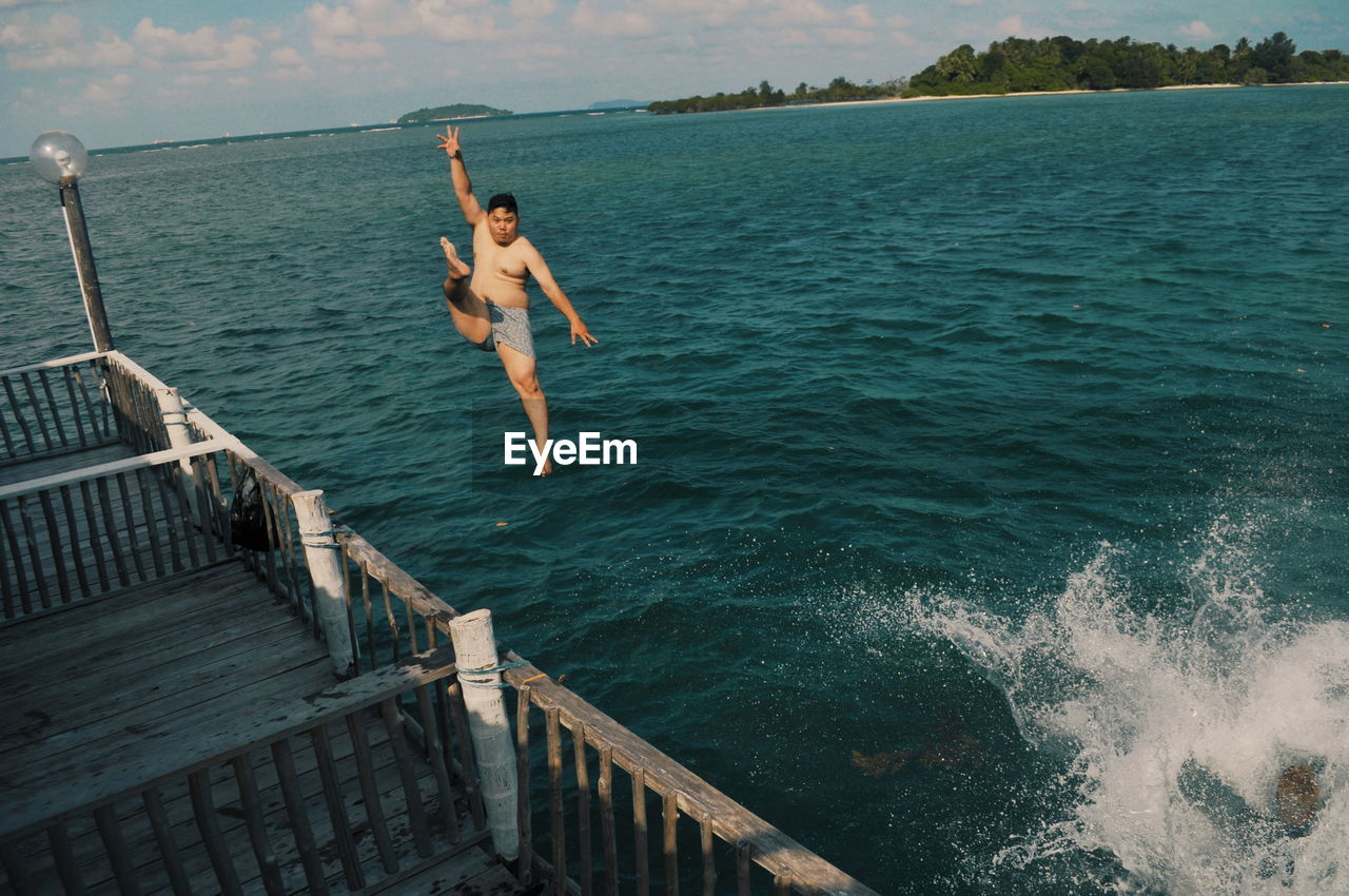 HIGH ANGLE VIEW OF PERSON JUMPING ON SEA AGAINST SKY