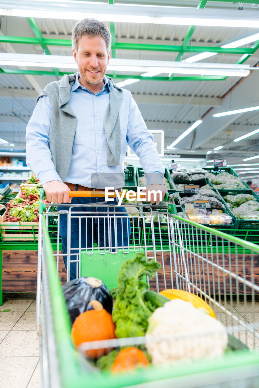 Man holding shopping cart with vegetables at supermarket