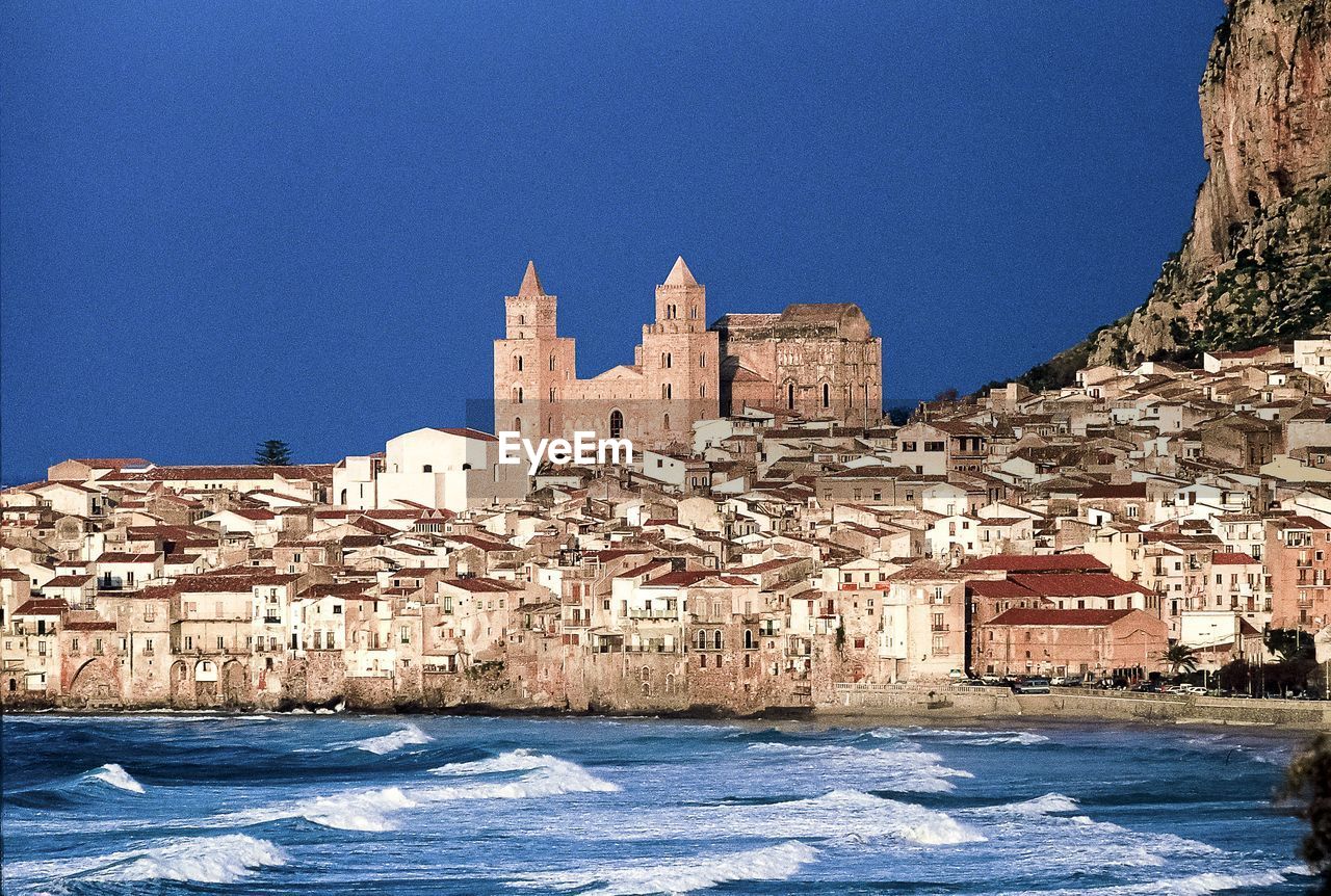Sea in front of cefalu cathedral in city against clear blue sky