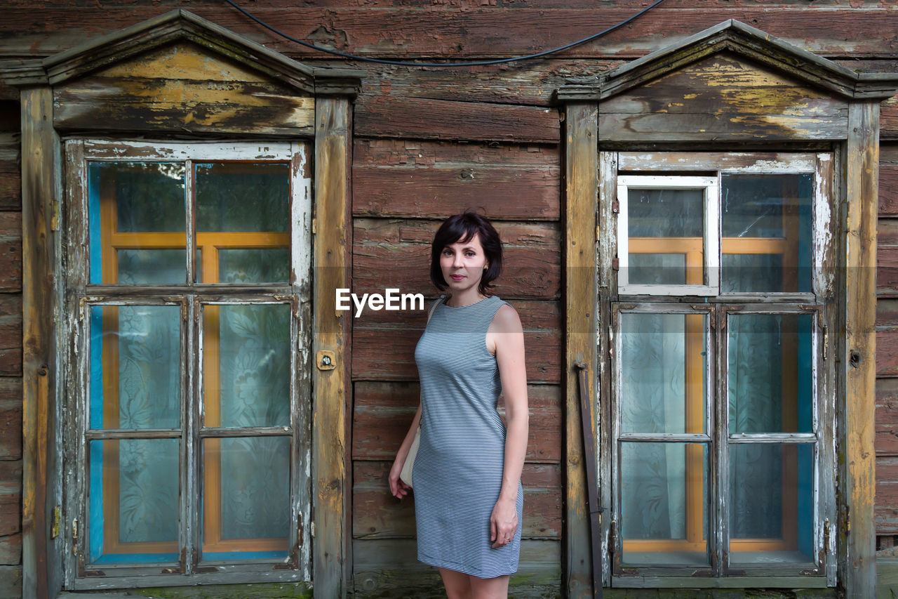 A brunette woman stands in an old wooden abandoned building.