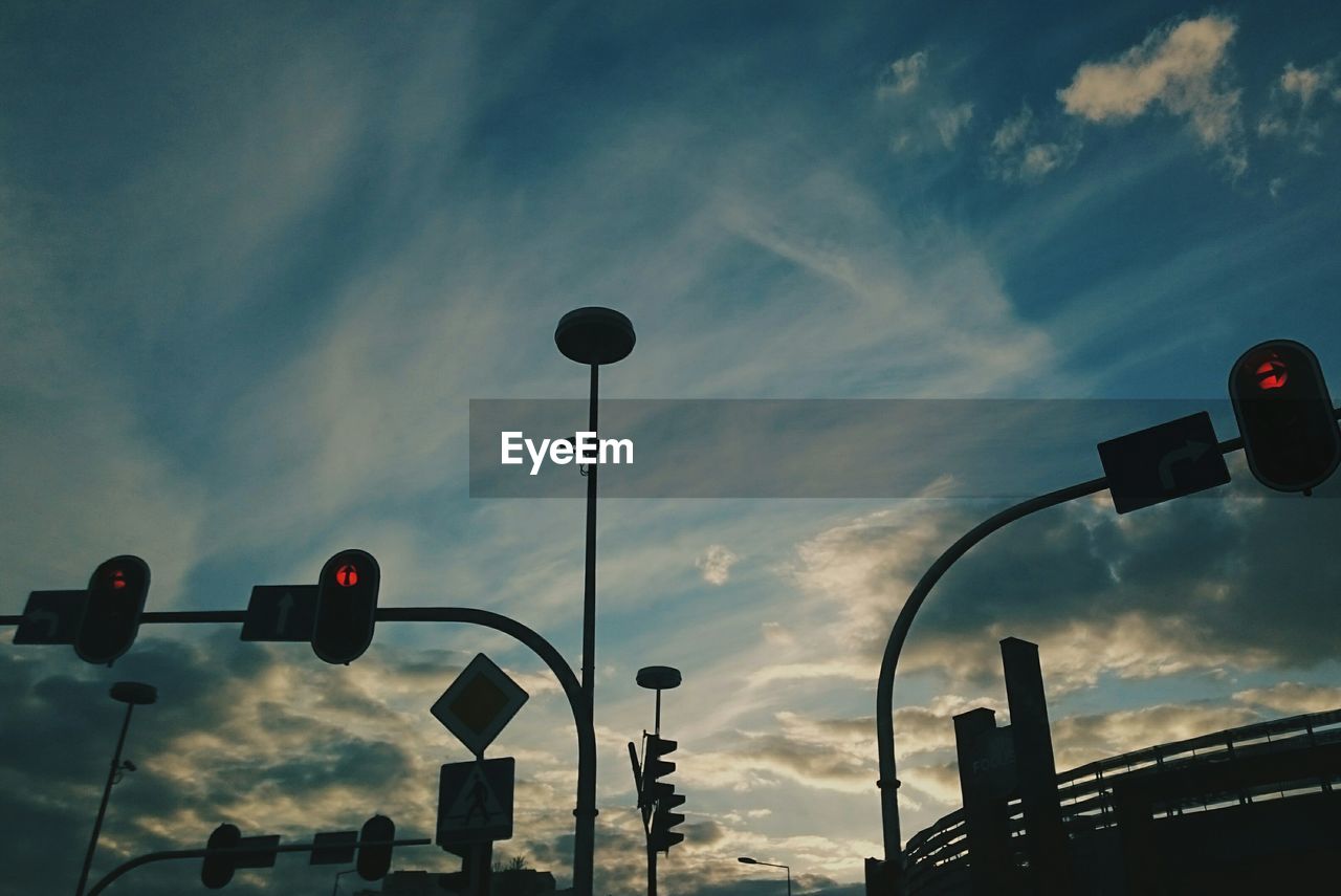 Low angle view of stoplights against cloudy sky